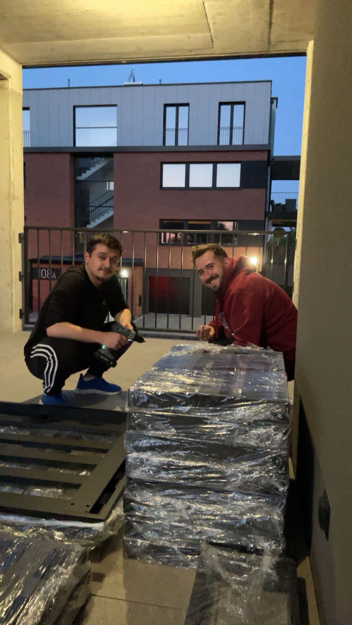 Dwóch mężczyzn skręca zafoliowane meble przed budynkiem o zmierzchu